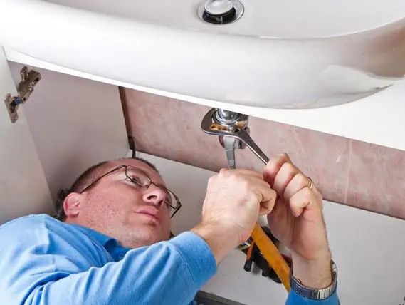 drain-repair plumber tightening a sink drain to repair a leak